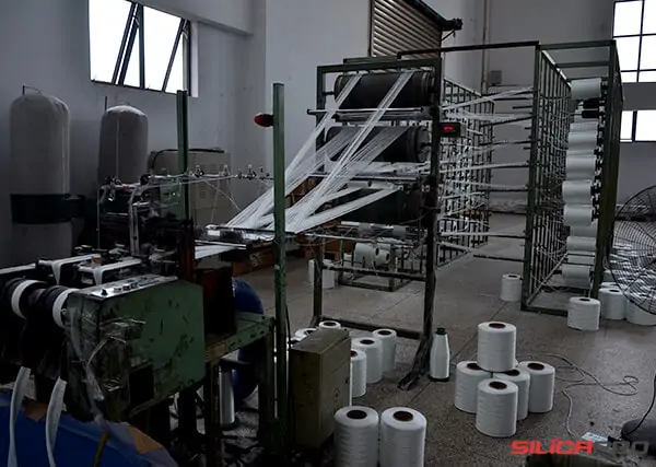Warping machine drawing treated silica yarn from a creel of bobbins